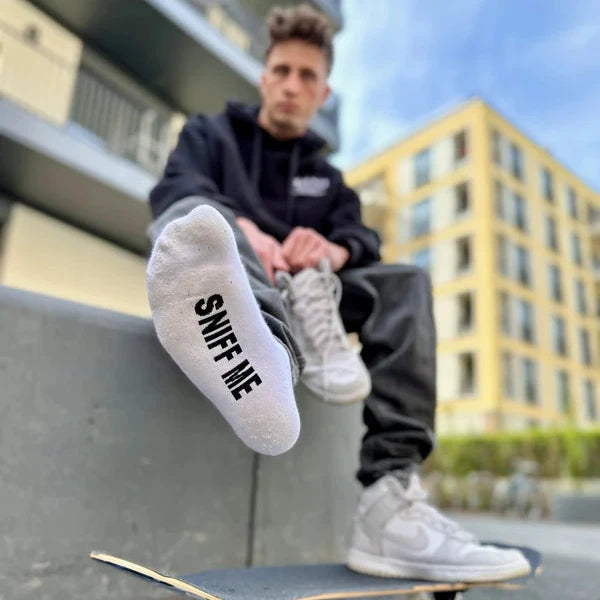 Person sitting on a skateboard with 'SNUFF ME' socks, blurred background