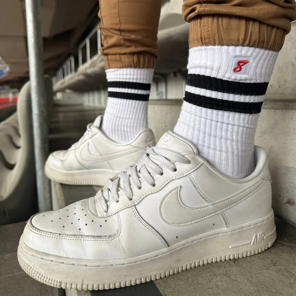 White sneakers worn with brown pants and white socks featuring a logo.