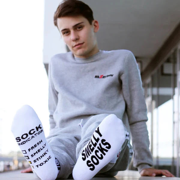 Person wearing a gray sweatshirt and white socks with text, sitting on a concrete surface.