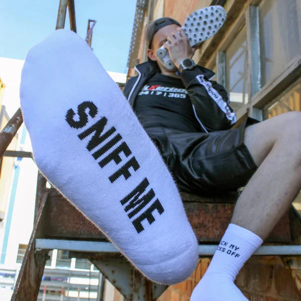 Person wearing 'SNIFF ME' socks sitting on a metal staircase.