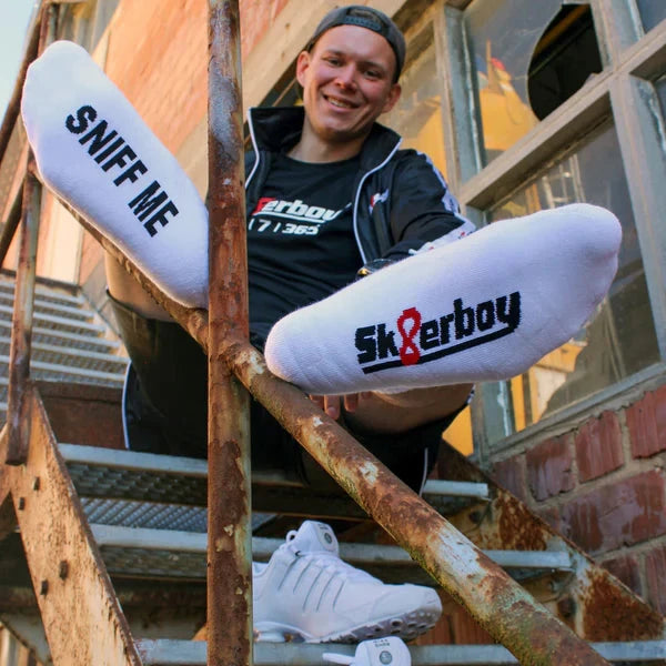 Person sitting on a metal staircase wearing white sneakers with 'Sk8erboy' branding.